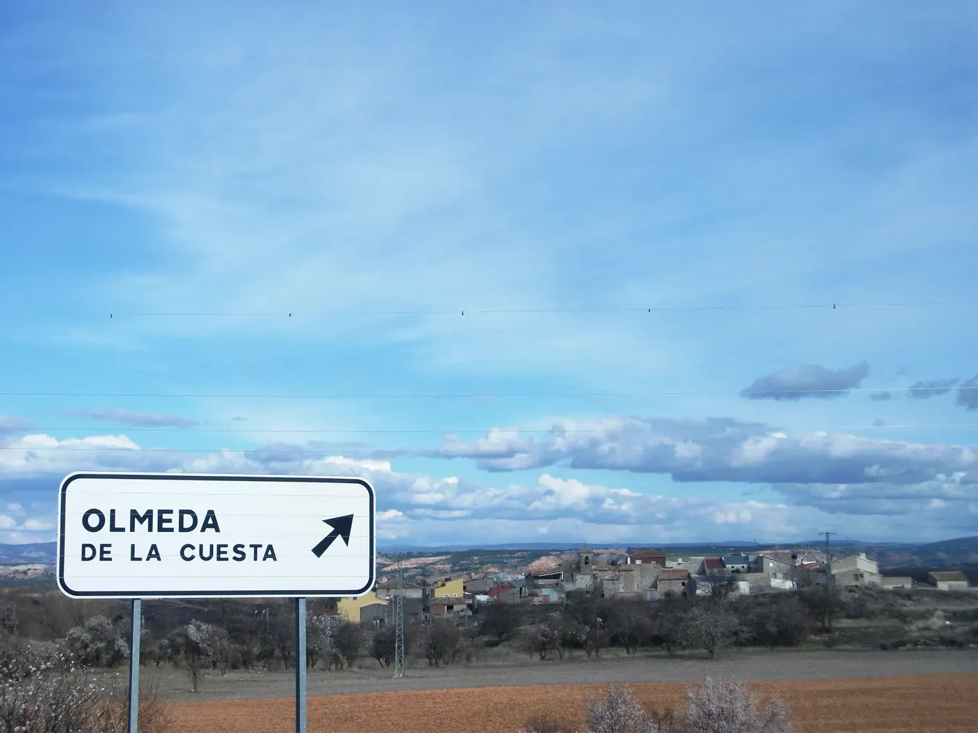 Cartel de carretera de Olmeda de la Cuesta con el pueblo al fondo